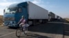 FILE - A local resident rides her bicycle as trucks are parked on a blocked road heading toward Crimea, in the village of Chaplinka, Ukraine, on Sunday, Sept. 20, 2015. 