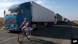 FILE - A local resident rides her bicycle as trucks are parked on a blocked road heading toward Crimea, in the village of Chaplinka, Ukraine, on Sunday, Sept. 20, 2015. 