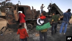 People look at weapons belonging to forces loyal to Libyan leader Muammar Gaddafi, destroyed by a coalition air strike, along a road between Benghazi and Ajdabiyah, March 23, 2011