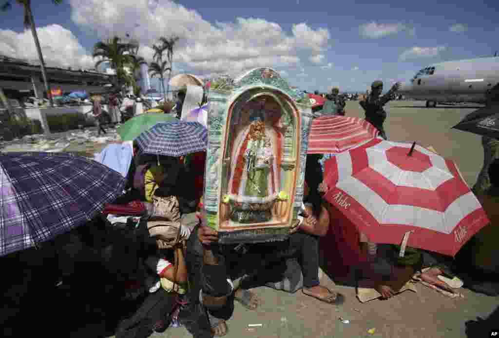 Typhoon survivor Rodrigo Villajos uses a figure of the Our Lady of Manaoag to shield him from the heat of the sun as he waits with others for the next military plane flight to Manila at Tacloban airport, Nov. 15, 2013. 