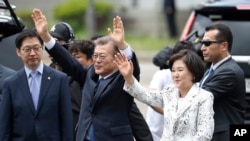 Nouvo Prezidan Kore di Sid la, Moon Jae-in, leve 2 men li pou l salye vwazen ak patizan li yo, devan palè prezidansyèl la nan Sewoul. Bò kote dwat li gen madanm li, Kim Jung-sook. Kore di Sid, 10 me 2017.