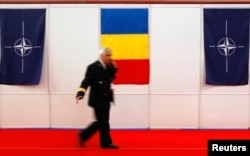 FILE - An officer walks past Romanian (C) and NATO flags during the International tri-service defense Exhibition and Conference dedicated to Defense, Aerospace, Homeland Security, Cyber Security and Safety and Security in Bucharest, May 15, 2014.