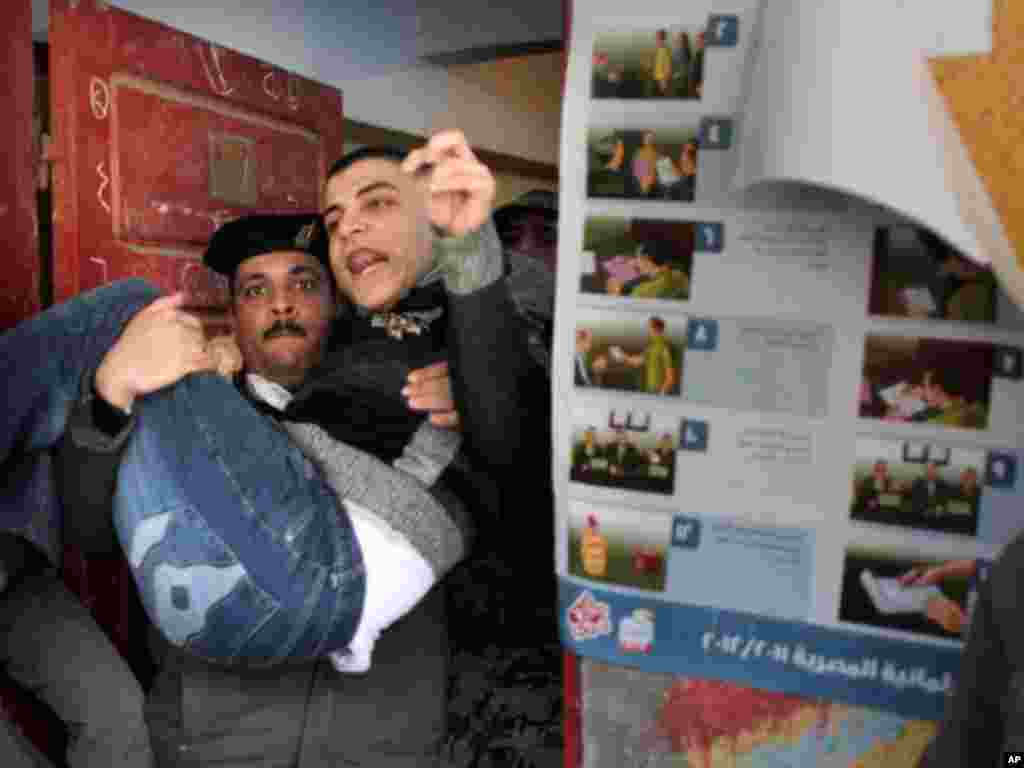 An Egyptian policeman carries a disabled man out of a polling center after voting in Qalyobeia on January 4, 2012. (AP)