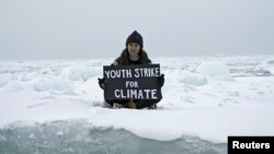 Aktivis lingkungan, Mya-Rose Craig, memegang spanduk bertuliskan "youth strike for climate" atau (pemuda mogok demi iklim" selagi duduk di atas es di tengah laut Arktik, September 2020 (Dok: REUTERS/Natalie Thomas)