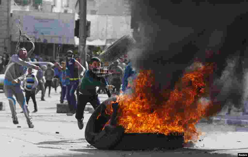 A young protester throws another tire onto a burning stack during clashes with Israeli troops following an anti-Israel demonstration in the West Bank city of Hebron, Nov. 14, 2014.