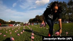 FILE - Patrice Sullivan, whose boyfriend, a Marine, died from suicide, helps to remove 5,000 small U.S. flags representing suicides of active and veteran members of the military line the National Mall, Wednesday, Oct. 3, 2018. (AP Photo/Jacquelyn Martin)
