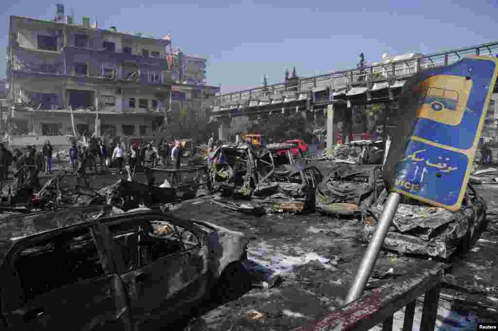 People walk near debris and damaged vehicles after an explosion in central Damascus February 21, 2013. Residents said that the big explosion shook the central Damascus district of al-Mazraa.