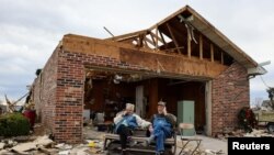 Warga tampak duduk di depan salah satu rumah yang hancur akibat tornado yang melanda wilayah Dawson Springs, Kentucky, minggu lalu. Foto diambil pada 15 Desember 2021. (Foto: Reuters/Evelyn Hockstein)