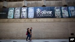 En esta fotografía de archivo de agosto de 2018, los peatones pasan frente al Banco Central mostrando una pancarta con los rostros en la nueva moneda del país, en Caracas, Venezuela.