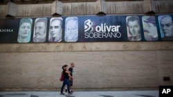 En esta fotografía de archivo de agosto de 2018, los peatones pasan frente al Banco Central mostrando una pancarta con los rostros en la nueva moneda del país, en Caracas, Venezuela.