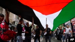 FILE—Palestinians carry a large national flag during a rally marking the 74h anniversary of what the Palestinians call the "Nakba," or "catastrophe" referring to their uprooting in the war over Israel's 1948 creation, in the West Bank city of Ramallah, May 15, 2022