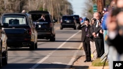 Un niño saluda al coche fúnebre que transporta el féretro, cubierto con la bandera estadounidense, del expresidente Jimmy Carter, mientras avanza por el centro de Plains, Georgia, el 4 de enero de 2025. 