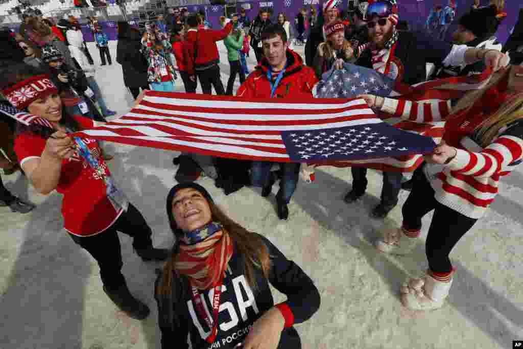 Para penggemar menari limbo di bawah bendera AS untuk merayakan kemenangan medali emas atlet Jamie Anderson dalam final snowboard slopestyle putri di Krasnaya Polyana, Rusia (9/2). (AP/Sergei Grits)