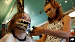 FILE - Robin Sotomayor, 5, wears a supergirl face mask as she gets her hair done by Haylee Cummins at Rockabetty's Hair Parlor, in Yuba City, Calif., May 4, 2020.