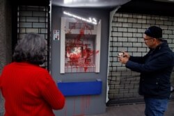 FILE - People use their phones to take pictures of an ATM machine damaged by anti-government protesters in Beirut, Lebanon, Jan. 15, 2020.