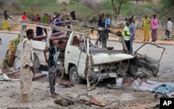 FILE - A Somali soldier, left, stands by the wreckage of a minibus that was destroyed in a suicide car bomb attack near the defense ministry compound in Mogadishu, Somalia, April 9, 2017.