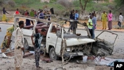 A Somali soldier, left, stands by the wreckage of a minibus that was destroyed in a suicide car bomb attack near the defense ministry compound in Mogadishu, Somalia, April 9, 2017.