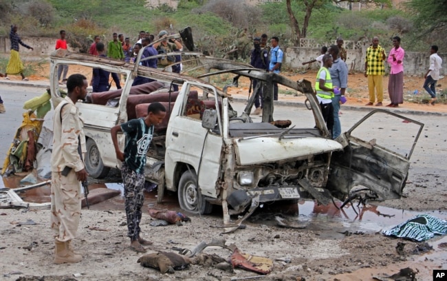 FILE - A Somali soldier, left, stands by the wreckage of a minibus that was destroyed in a suicide car bomb attack near the defense ministry compound in Mogadishu, Somalia, April 9, 2017.