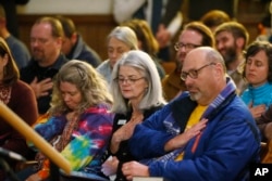 Vicki Cowart, center, executive director of Planned Parenthood of the Rocky Mountains, joins others in putting their hands on their hearts at All Souls Unitarian Universalist Church in Colorado Springs, Colo., during a vigil for victims of Friday's shooting, Nov. 27, 2015.
