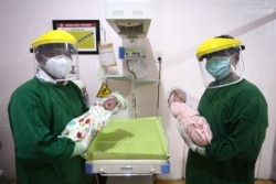 Para dokter mengenakan alat pelindung diri menggendong bayi baru lahir yang mengenakan pelindung wajah sebagai tindakan perlindungan di tengah pandemi COVID-19 di sebuah klinik di Bireuen, Aceh, 15 April 2020. (Foto: AFP/Amanda Jufrian)