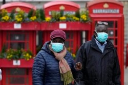 Para pejalan kaki mengenakan masker saat melewati kotak telepon di Uxbridge, London, Senin, 10 Januari 2022. (AP Photo/Frank Augstein)