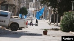 ປະຊາຊົນຖືຄຸ ໃນຂະນະທີ່ພວກເຂົາເຈົ້າຍ່າງຜ່ານຖະໜົນທີ່ໄດ້ຮັບຄວາມເສຍຫາຍ ໃກ້ກັບຜ້າສີຟ້າທີ່ຖືກໃຊ້ເປັນບ່ອນລີ້ຈາກດັກຍິງ ຫຼື snipers ໃນເມືອງ Manbij, ບໍລິເວນຂອງນະຄອນຫຼວງ Aleppo ທີ່ຄວບຄຸມໂດຍລັດຖະບານ. ຊີເຣຍ. 7 ສິງຫາ, 2016. 