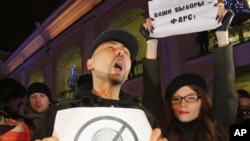 Opposition activists, one of them holding a poster depicting Russian Prime Minister Vladimir and another a poster reading, "Your election is a farce", shout slogans during a protest against vote rigging in St. Petersburg, Russia, December 4, 2011.