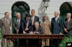 1993 Mideast Peace Agreement: Israeli Foreign Minister Shimon Peres signs the Mideast Peace Agreement on the South Lawn of the White House in Washington, D.C., as President Clinton, standing center, PLO Chairman Yasser Arafat, third from right, and other dignitaries look on, Sept. 13, 1993. From left to right are: Russian Foreign Minister Andrei Kozyrev; Israeli Prime Minister Yitzhak Rabin; an unidentified aide; Clinton; Peres; Arafat; Secretary of State Warren Christopher; and Arafat aide Mahmoud Abbas.