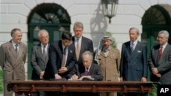 1993 Mideast Peace Agreement: Israeli Foreign Minister Shimon Peres signs the Mideast Peace Agreement on the South Lawn of the White House in Washington, D.C., as President Clinton, standing center, PLO Chairman Yasser Arafat, third from right, and other