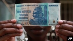 FILE - A woman holds a 100 trillion-dollar note in Harare, the highest denomination printed by the Reserve Bank of Zimbabwe. 