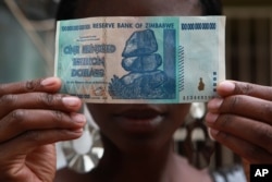 FILE - A woman holds a 100 trillion-dollar note in Harare, the highest denomination printed by the Reserve Bank of Zimbabwe.