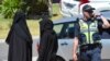 Hai người phụ nữ đứng bên cạnh một cảnh sát đang chặn một con đường để khám xét một căn nhà ở Meadow Heights, ngoại ô Melbourne, Australia, 23/12/2016.