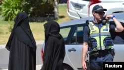 Two women stand next to a policeman blocking a road where police officers are searching a house in the Melbourne suburb of Meadow Heights, Australia, Dec. 23, 2016.