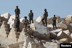 FILE - Syrian army soldiers stands on the ruins of the Temple of Bel in the historic city of Palmyra, in Homs Governorate, Syria, April 1, 2016.