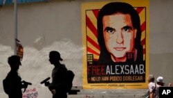 Dos personas hablan en Caracas, Venezuela, frente a un cartel que exige la liberación de Alex Saab, actualmente procesado en Estados Unidos.