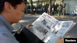 FILE - A Chinese visa applicant reads a Beijing newspaper as he waits outside the U.S. Embassy.