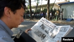 FILE - A Chinese visa applicant reads a Beijing newspaper as he waits outside the U.S. Embassy compound.