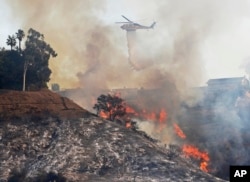 A Los Angeles County Fire Department helicopter makes a water drop on flames sweeping up a steep canyon wall, threatening homes on a ridge line after the Skirball wildfire swept through the Bel Air district of Los Angeles, Wednesday, Dec. 6, 2017.