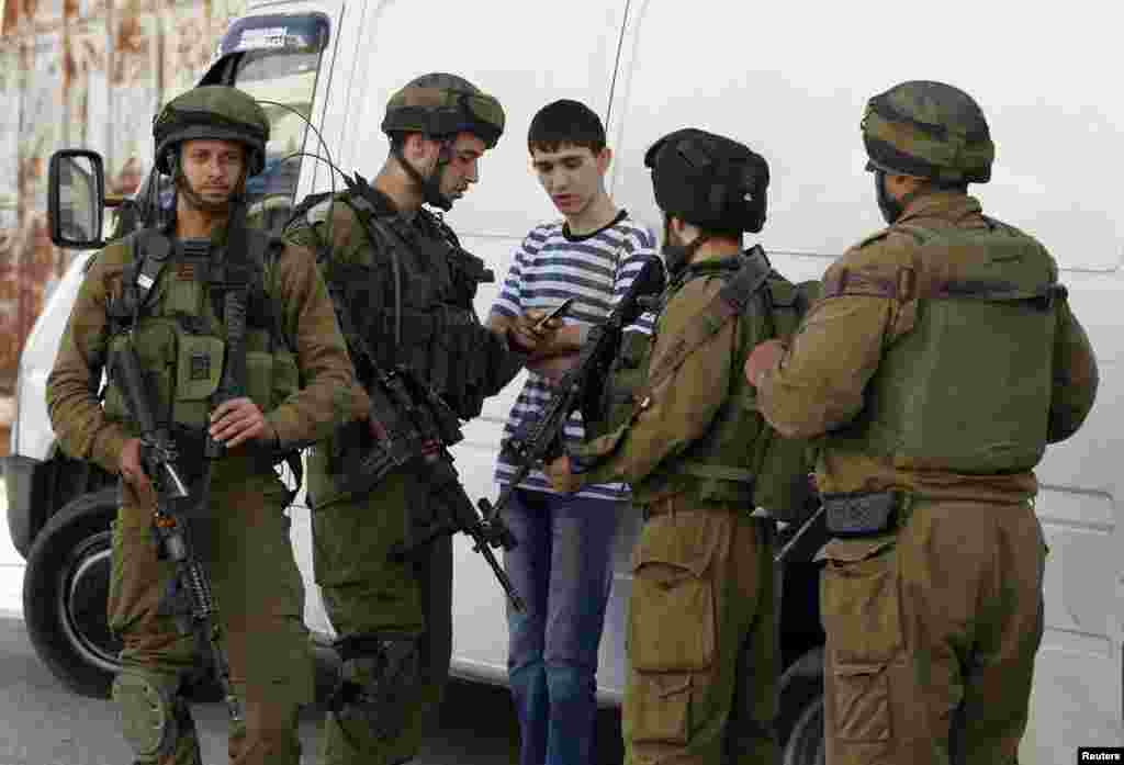 Israeli soldiers search a Palestinian youth during an operation to locate three Israeli teens in the West Bank city of Hebron, June 16, 2014. 