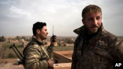 U.S.-backed Syrian Democratic Forces (SDF) fighters talk on a radio in a rooftop position as fight against Islamic State militants continues in the village of Baghouz, Syria, Feb. 16, 2019.