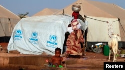 A woman walks past a child playing with water in a refugee camp in Sevare, Mali, Jan. 26, 2013. 