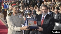 Egypt's new President Mohamed Morsi (R) poses with a gift from Field Marshal Mohamed Tantawi (L), head of Egypt's ruling Supreme Council of the Armed Forces (SCAF), during a ceremony where the military handed over power to Morsi at a military base in Hiks