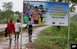 FILE - People walk past a billboard warning residents to stop the stigmatization of Ebola survivors, in Kenema, eastern Sierra Leone, Aug. 12, 2015.