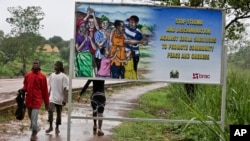 FILE - People walk past a billboard warning residents to stop the stigmatization of Ebola survivors, in Kenema, eastern Sierra Leone. On Nov. 7, WHO will declare the country is Ebola-free after going 42 days without any new infections.