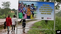 FILE - People walk past a billboard warning residents to stop the stigmatization of Ebola survivors, in Kenema, eastern Sierra Leone, Aug. 12, 2015.