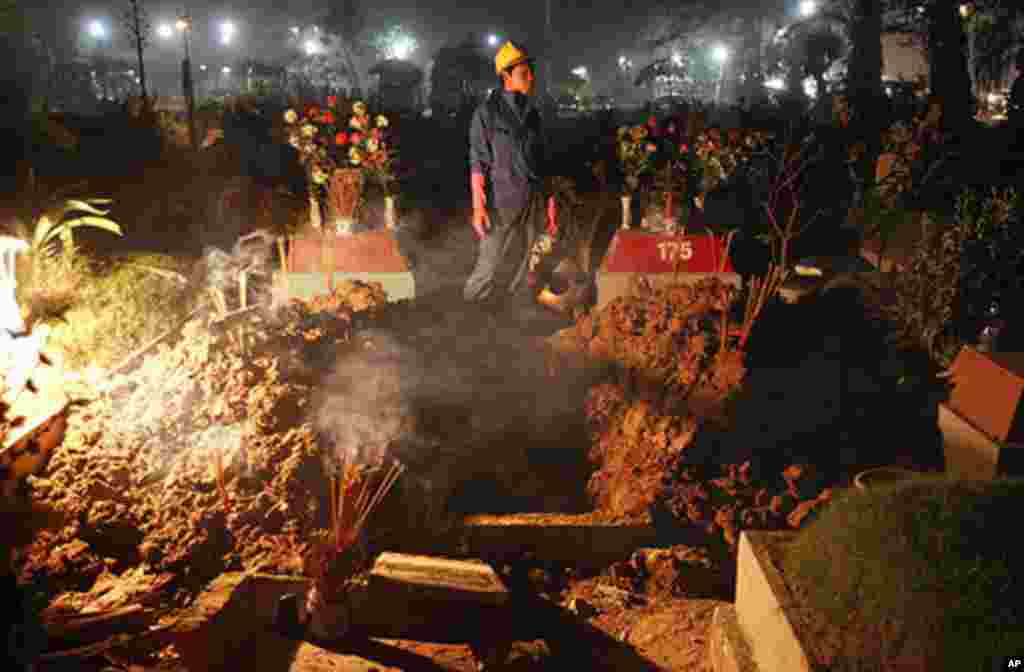 A worker stands at a grave before a reburial ritual at Van Dien cemetery in Hanoi December 19, 2011. The ritual is held just before dawn, three years after death and relatives dig up the grave of their dead, clean their bones, and take them to a new buria