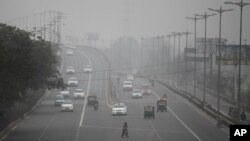 Seorang perempuan India menyeberang jalan di tengah kabut asap atau smog di New Delhi.