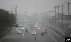 FILE - An Indian woman crosses a road as vehicles move through morning smog on the last day of a two-week experiment to reduce the number of cars to fight pollution in New Delhi, Jan. 15, 2016.