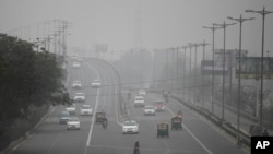 FILE - A pedestrian and vehicles move through morning smog in New Delhi, Jan. 15, 2016.