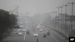 FILE - An Indian woman crosses a road as vehicles move through morning smog on the last day of a two-week experiment to reduce the number of cars to fight pollution in New Delhi, Jan. 15, 2016. 